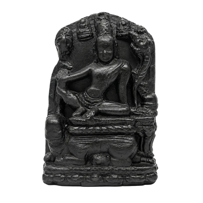 A small black stone or resin statue of a seated Buddha figure with ornate halo-like details behind it, photographed against a plain white background.